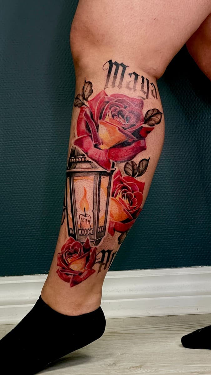 Color calf tattoo with three red roses and a lantern with a lit candle, framed by black lettering above and below.