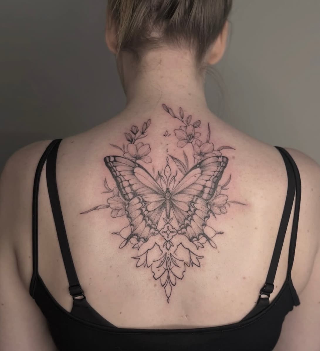 Delicate butterfly and floral tattoo in fine line black and grey on the forearm